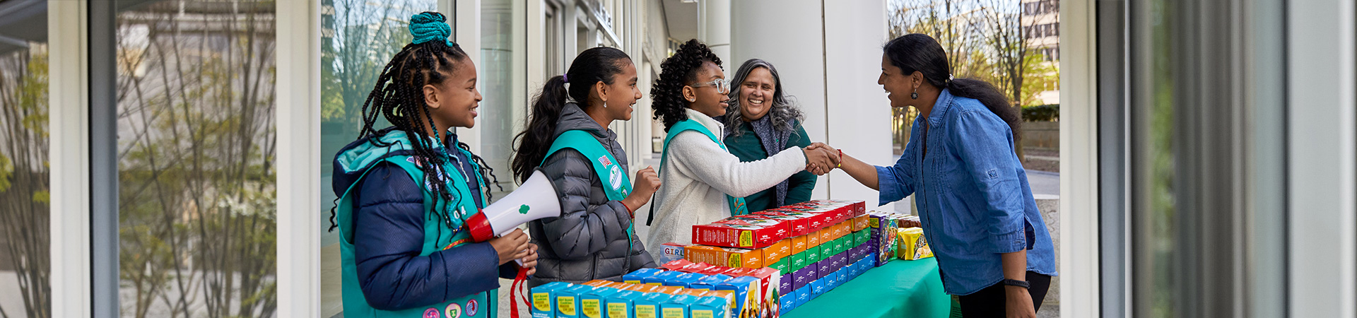  girl scouts selling cookies with one girl in front of booth holding sign that says "girl scout cookie proceeds stay local" 